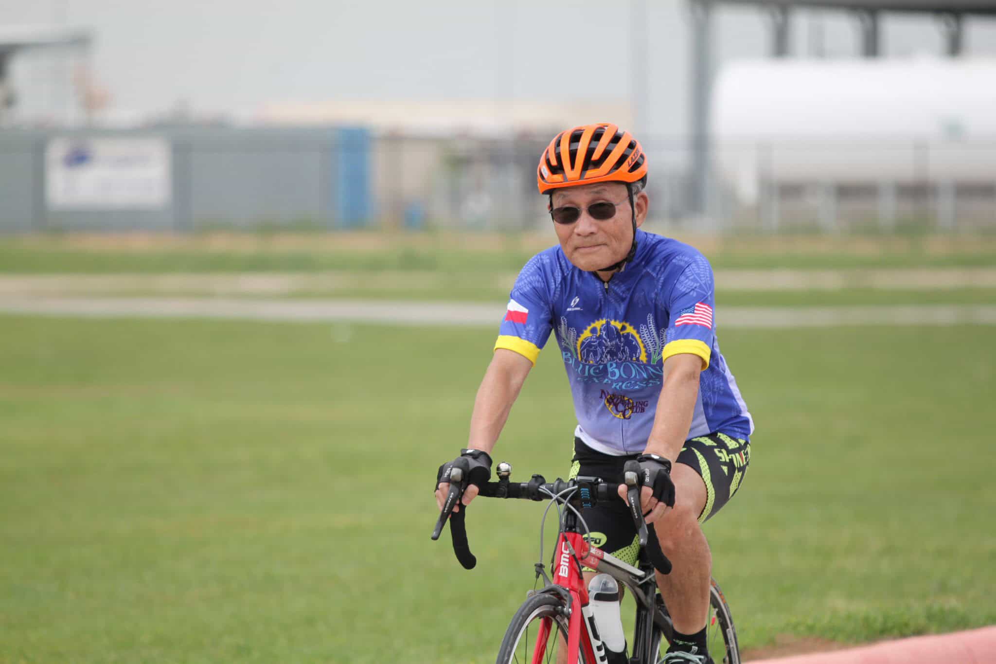 Elderly man riding a red bicycle outdoors in a park setting for Bluebonnet Express.