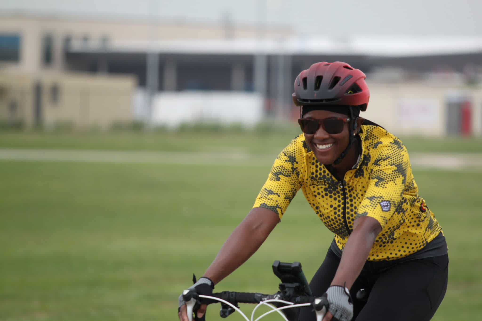 Bright cyclist wearing a red helmet and sunglasses riding a bike outdoors on a sunny day.
