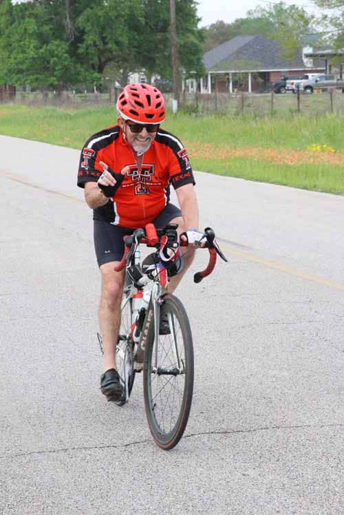 Brightged bicycle rider with helmet smiling on road, sportswear, and bike, enjoying Bluebonnet Express ride.
