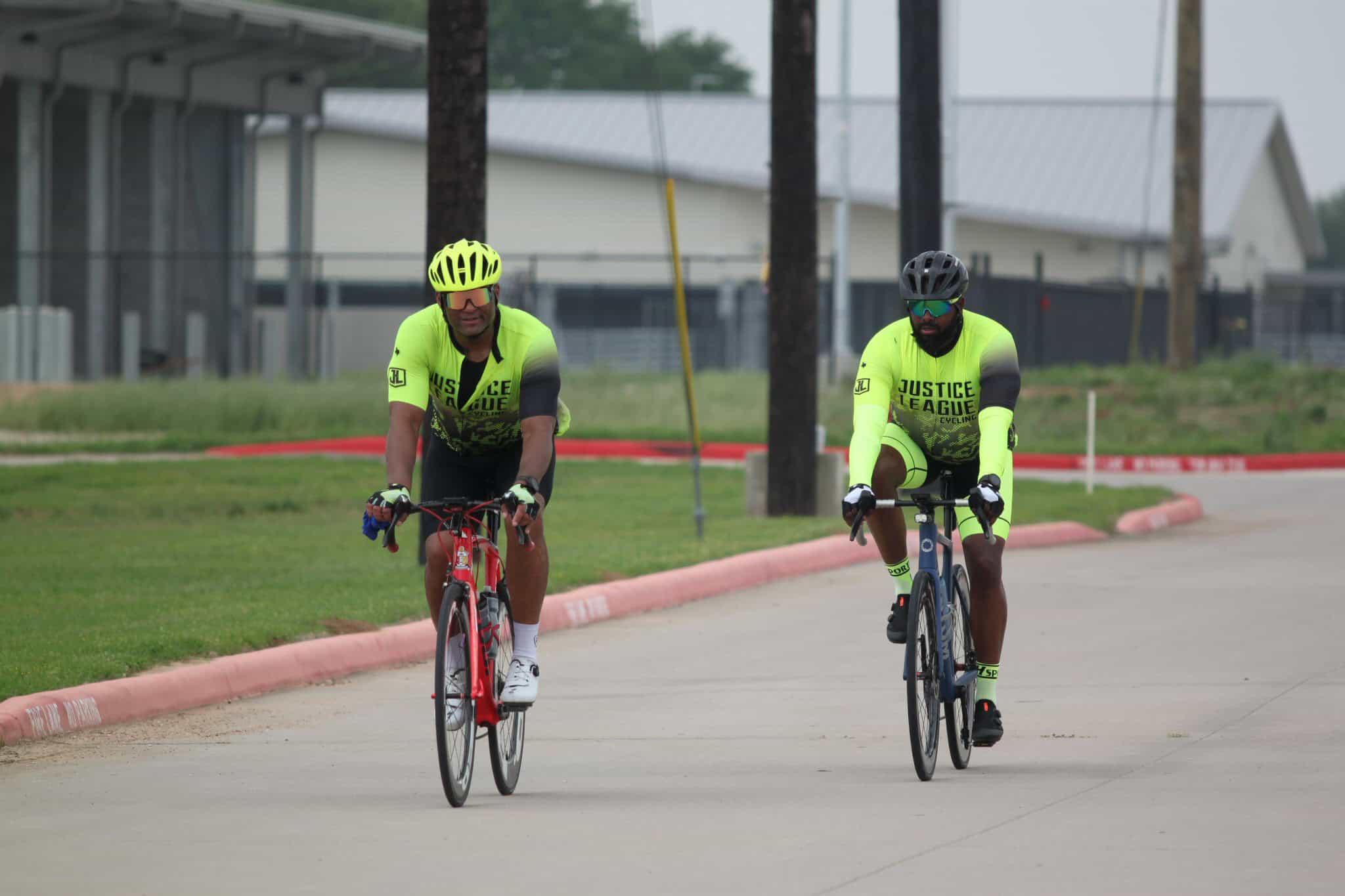 Bright yellow cycling jerseys with "Justice League" logo on team of two men riding bikes.
