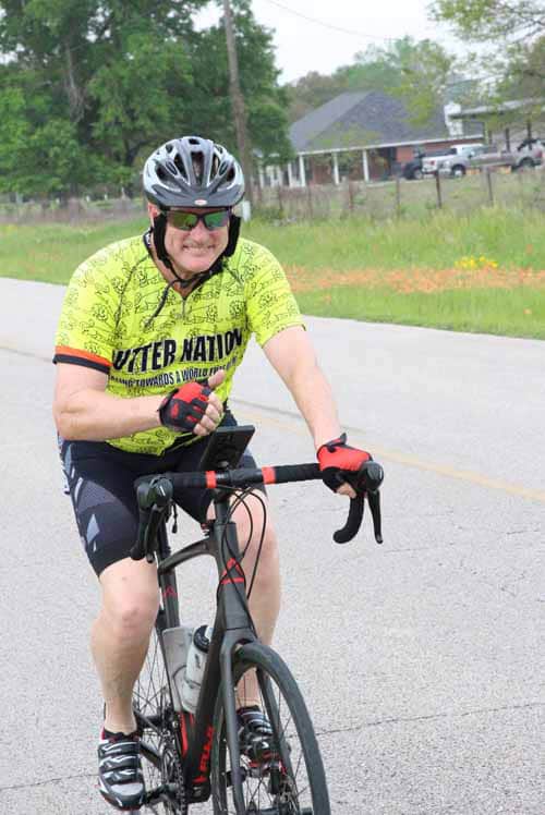 Happy cyclist riding on the road in a yellow jersey and helmet, enjoying a ride with Bluebonnet Express.