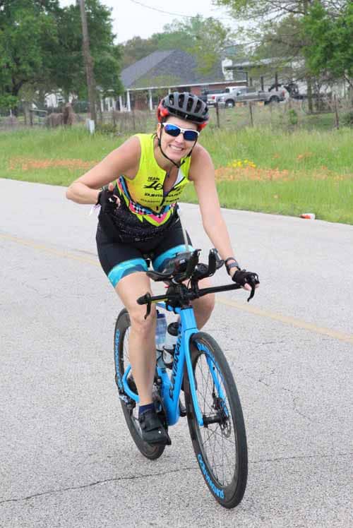 Smiling woman riding a blue mountain bike on a rural road during daytime.