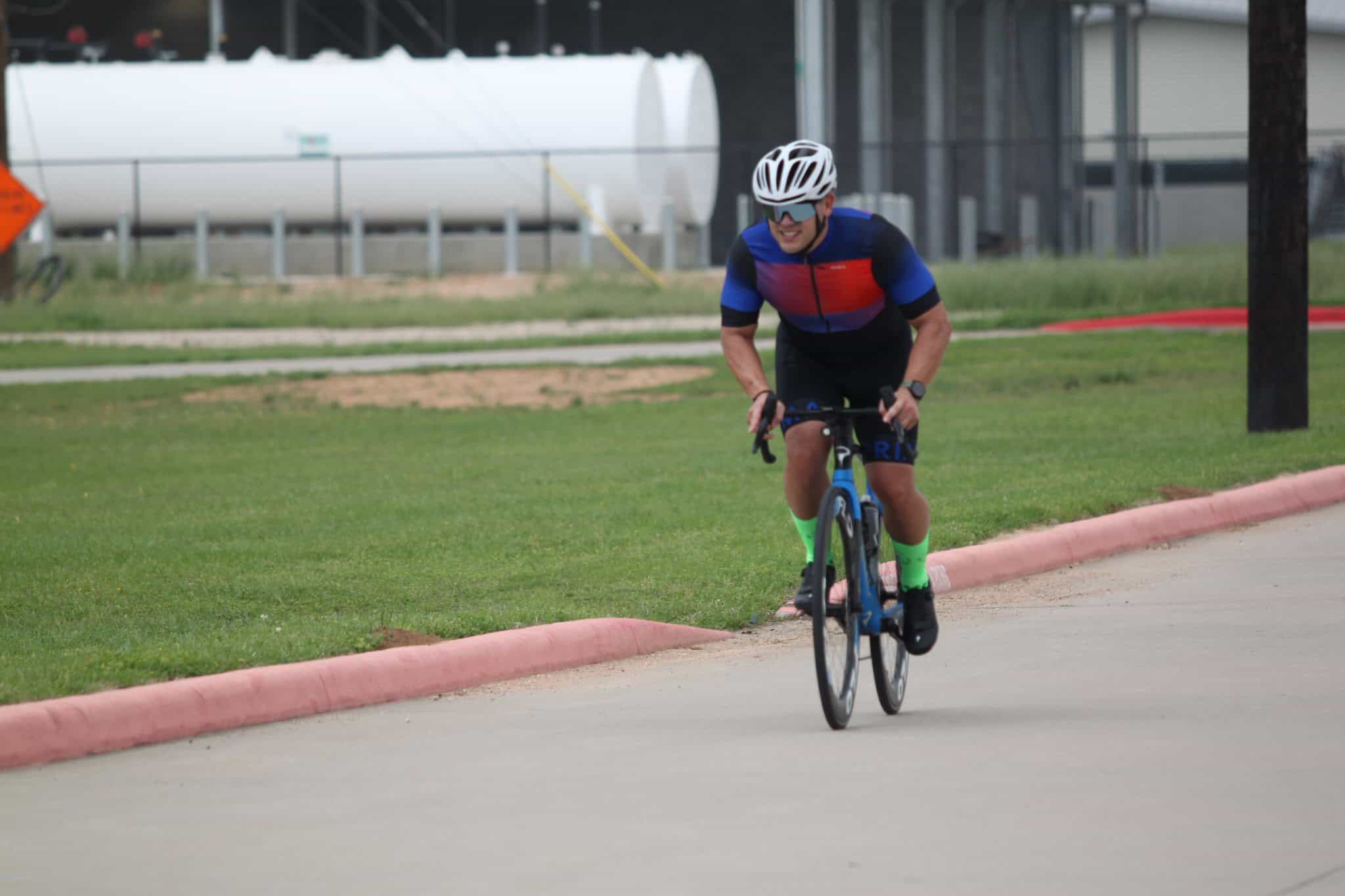 Bright male cyclist riding on a paved road, wearing a colorful cycling jersey, helmet, and neon green socks for Bluebonnet Express event.