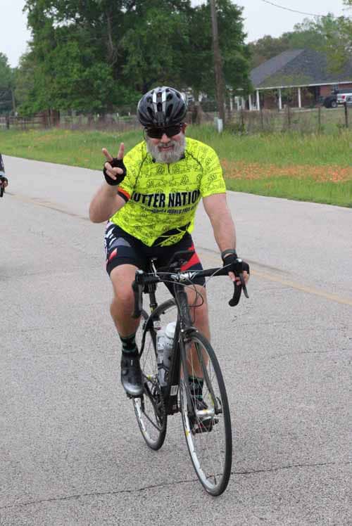 Smiling cyclist wearing a bright yellow jersey and riding on rural road during Bluebonnet Express event.