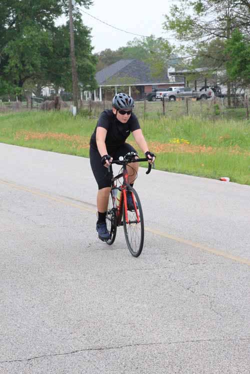Bike rider in black cycling gear on a rural road, enjoying scenic outdoor biking adventure.