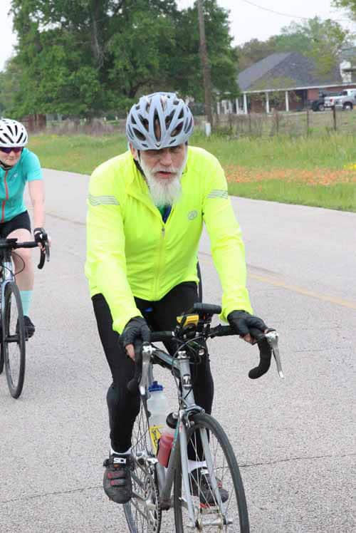 Older man cyclist wearing yellow jacket riding on country road during daytime.