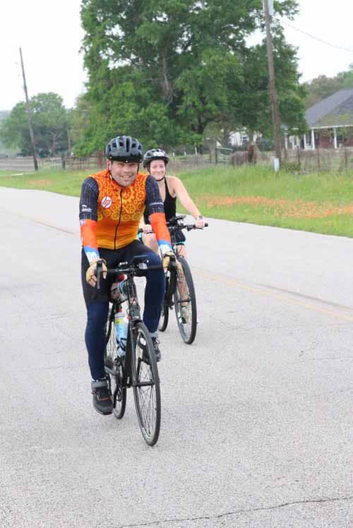 Brightly dressed cyclists enjoying a ride on a scenic rural road with lush greenery and trees in the background.