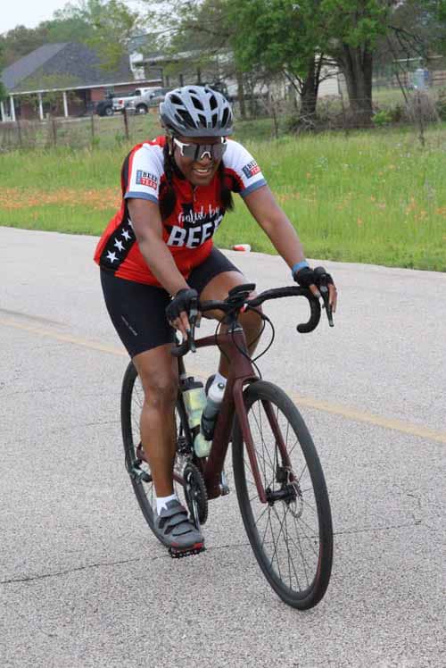 Bright cyclist wearing Bluebonnet Express jersey riding a road bike on street at daytime.