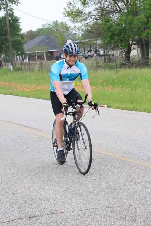 Bright cyclist riding on a scenic rural road during daytime, promoting Bluebonnet Express cycling event.