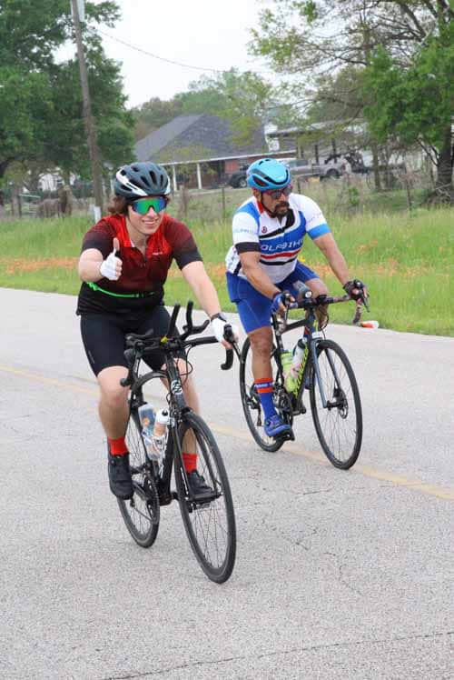 Brightly colored cyclists riding on a scenic road during daytime with trees and houses in the background.