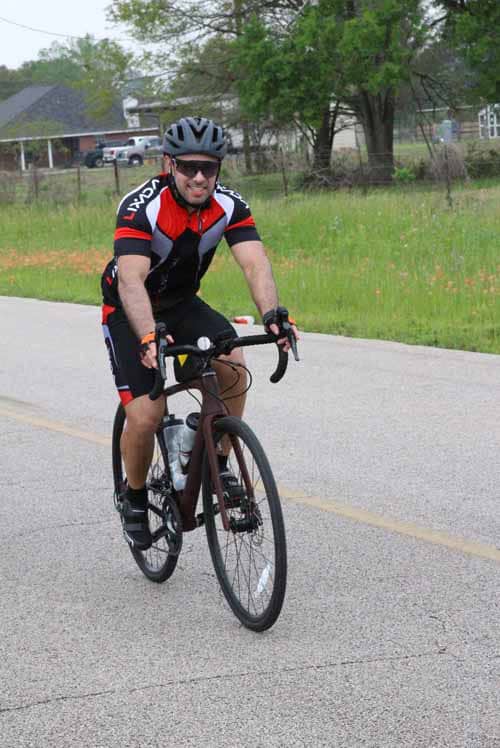 Man riding a road bike on a rural street in cycling gear, enjoying a sunny outdoor ride.