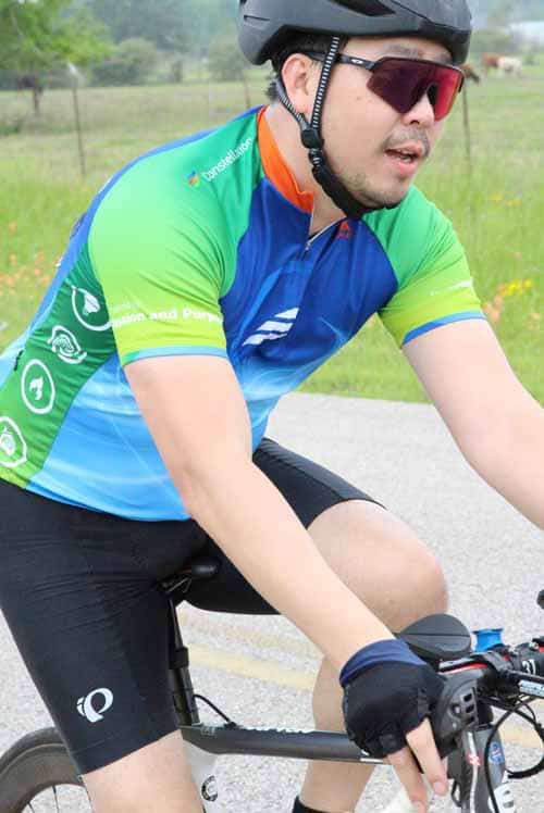 Bright blue and green cyclist jersey with safety features, riding outdoors on a scenic trail.