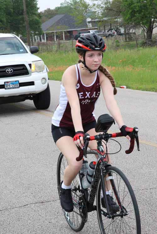 Young girl cyclist wearing helmet riding bike on road during daytime.