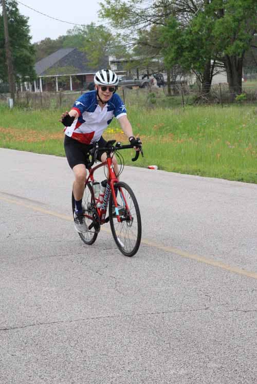 Cyclist riding a bike on a rural road, wearing a helmet and sunglasses, promoting outdoor cycling activities.