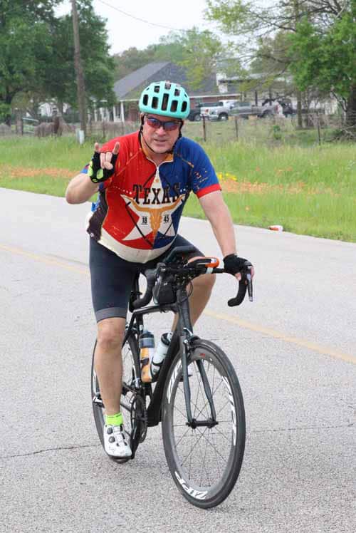 Cyclist riding on the road with a blue helmet and Texas-themed jersey, promoting Bluebonnet Express cycling event.