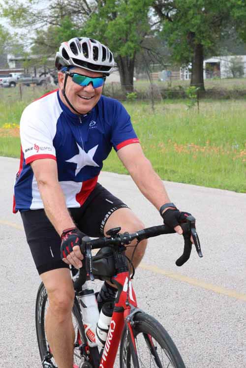 Bright smiling cyclist with helmet and sunglasses riding on a scenic outdoor road.