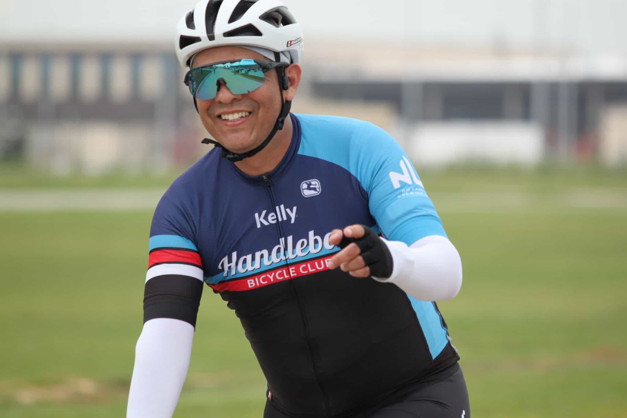 Bright smiling cyclist wearing Bluebonnet Bicycle Club jersey and sunglasses, enjoying outdoor ride.