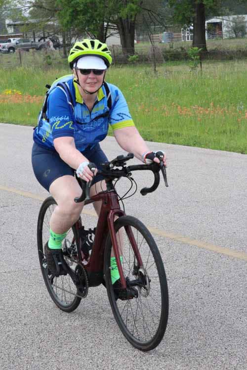 Bright woman cycling on a road bike wearing helmet and sunglasses for safety and outdoor exercise.