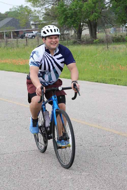 Bright smiling cyclist riding blue bike on open road during daytime.