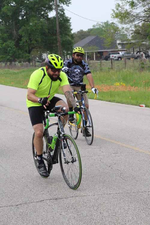 Bright yellow cycling helmets and jerseys on two cyclists riding along a rural road.