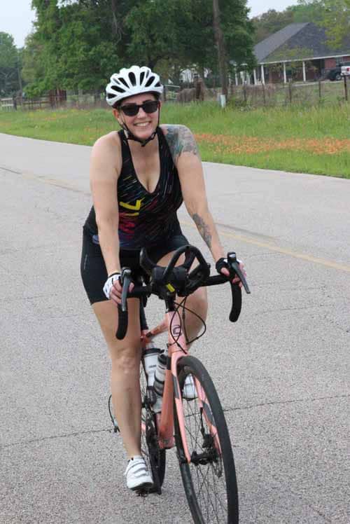 Smiling woman riding a pink bicycle wearing a white helmet and sunglasses.