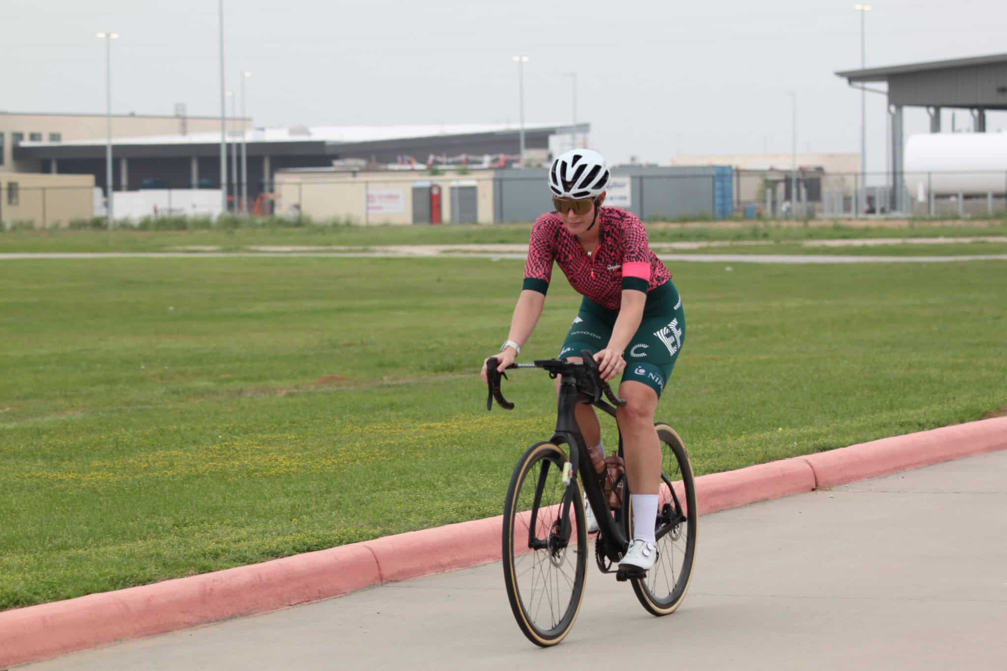 Stylish cyclist riding a black bike outdoors on a grassy path, promoting Bluebonnet Express cycling events.