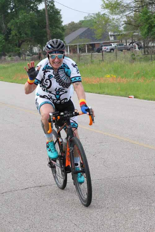 Vibrant cyclist enjoying Bluebonnet Express ride on scenic Texas road with colorful gear and cheering smile.