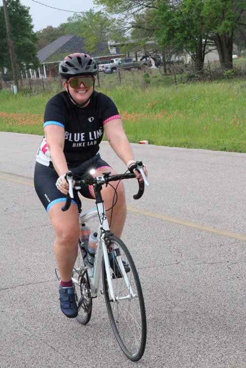 Bright female cyclist wearing Blue Bonnet Express biking jersey on road, enjoying outdoor cycling event.