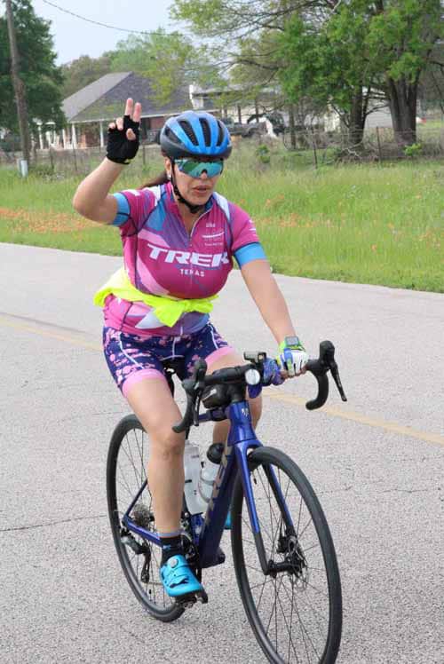 Bright female cyclist wearing pink and blue gear, riding a road bike on a suburban street.