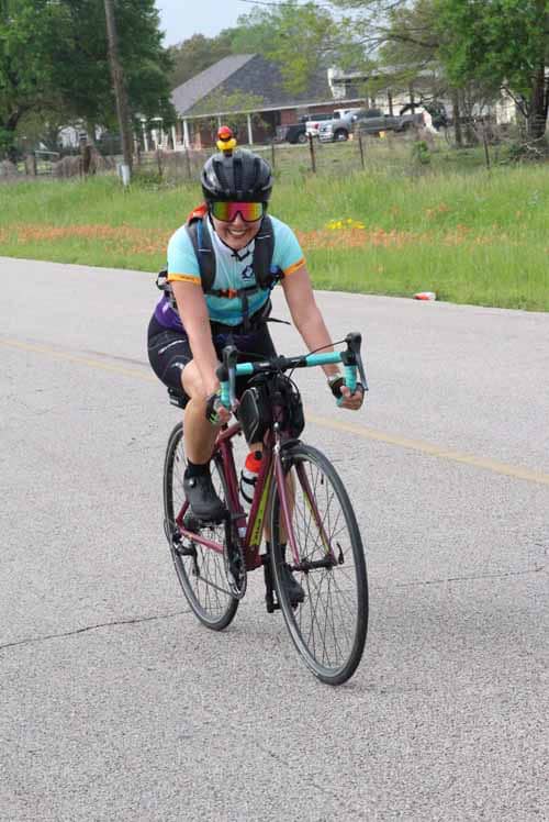 Bright female cyclist riding on rural road during Bluebonnet Express event, wearing helmet and sunglasses.