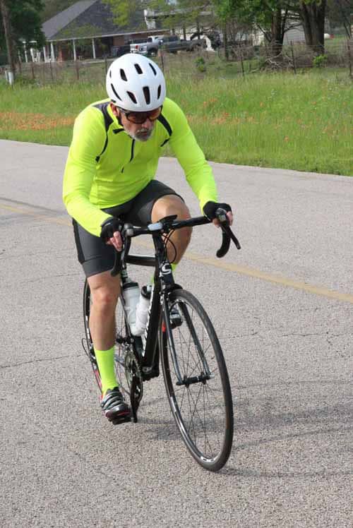 Man cycling on the road wearing bright yellow sportswear and helmet.