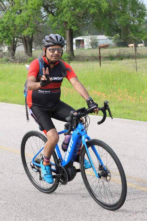 Happy cyclist riding blue bike on scenic outdoor trail with trees and open fields.
