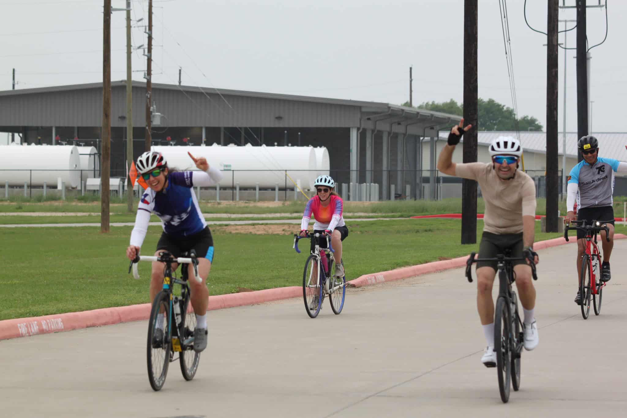 Brightly dressed cyclists riding bikes on a paved path during daytime, promoting Bluebonnet Express cycling event.