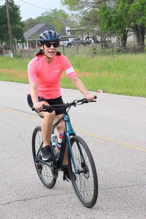 Bright woman riding Bluebonnet Express bike in scenic outdoor setting.