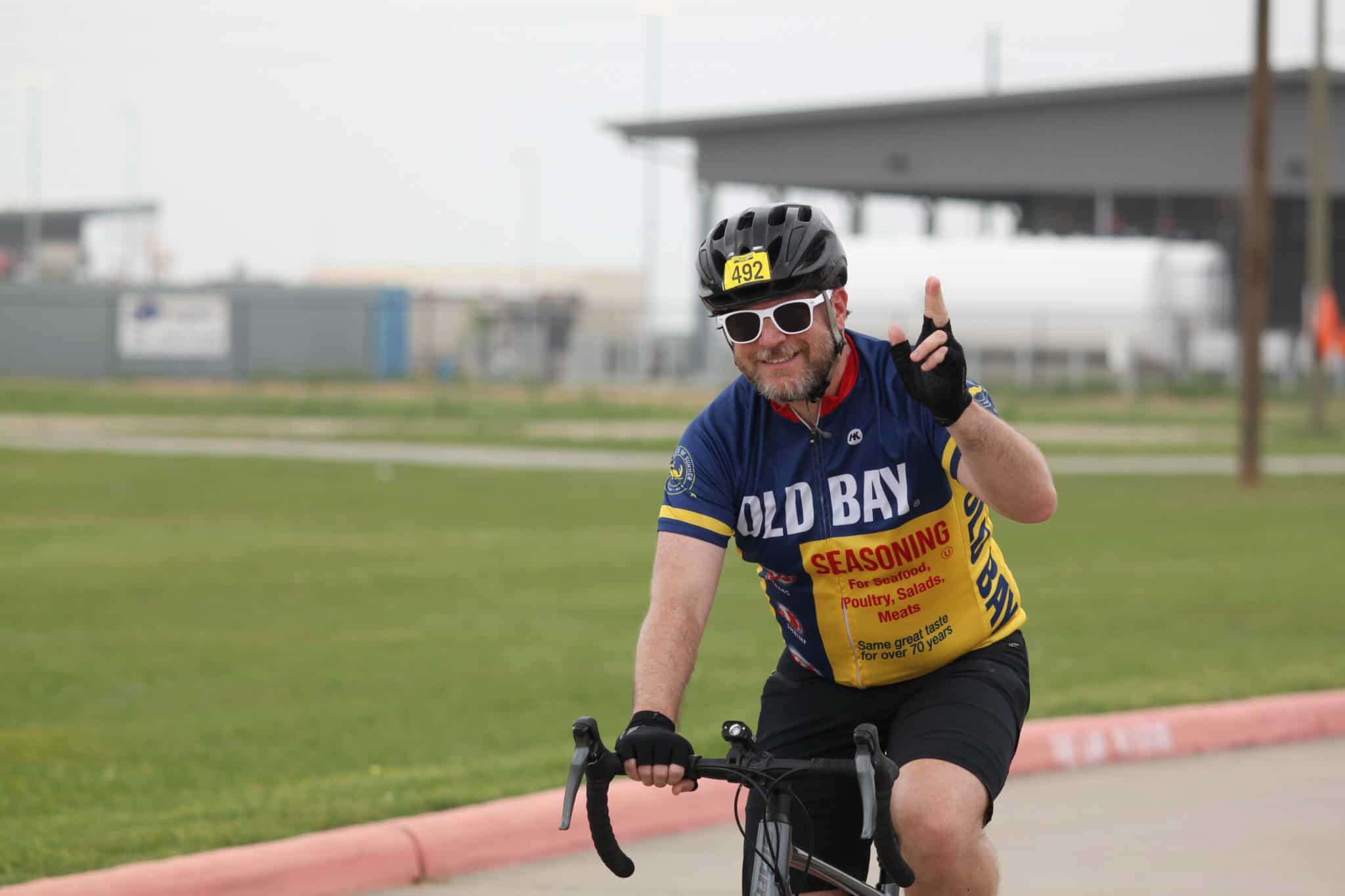 Bright cyclist wearing Old Bay jersey, cycling outdoors, smiling, celebrating.