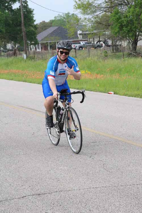 Bright blue cyclist jersey, smiling man on road bike, outdoors in pleasant weather for Bluebonnet Express.