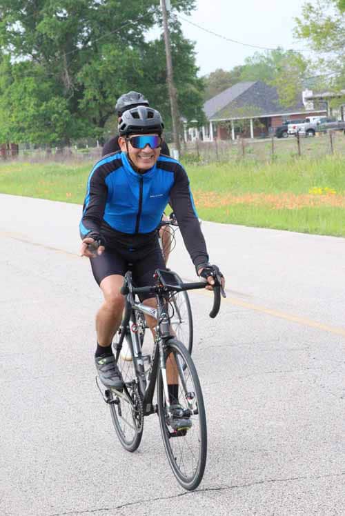 Helmeted cyclist riding on the road with greenery in the background.