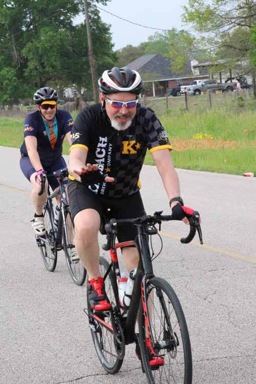 Happy cyclists riding on a scenic road during Bluebonnet Express event, enjoying outdoor cycling and Texas wildflowers.