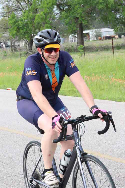 Vibrant cyclist riding on scenic rural road with green trees, promoting Bluebonnet Express bike events and outdoor cycling.