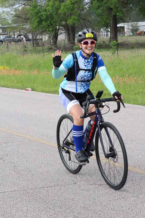 Vibrant cyclist riding on the road with Bluebonnet Express bike gear and smiling cheerfully.