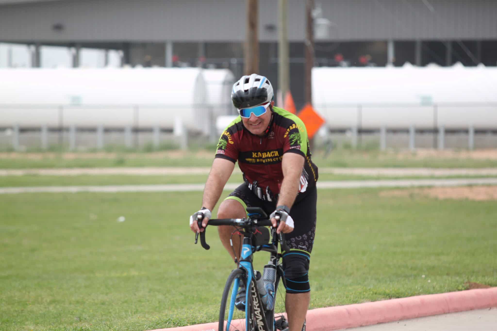 Vibrant cyclist wearing helmet and sunglasses riding bike on grassy trail, showcasing Bluebonnet Express biking event.