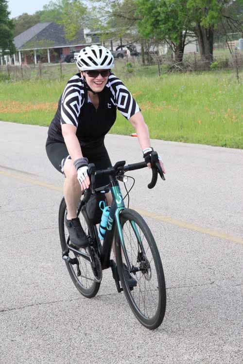 High-quality image of woman cyclist smiling on a scenic bike route, promoting Bluebonnet Express cycling event and eco-friendly transportation.