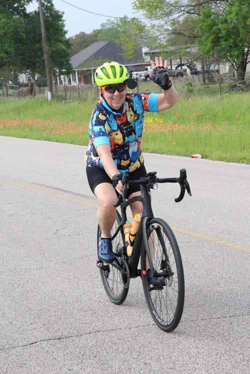 Bike rider wearing colorful Pokémon jersey, green helmet, and sunglasses riding on suburban street.
