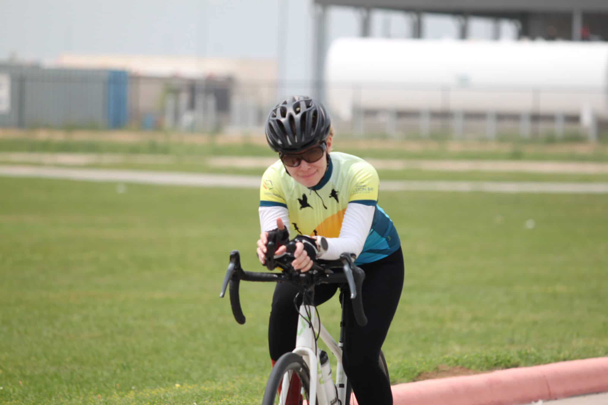 Bright cyclist wearing helmet and sunglasses riding a bike outdoors on a green grassy field.