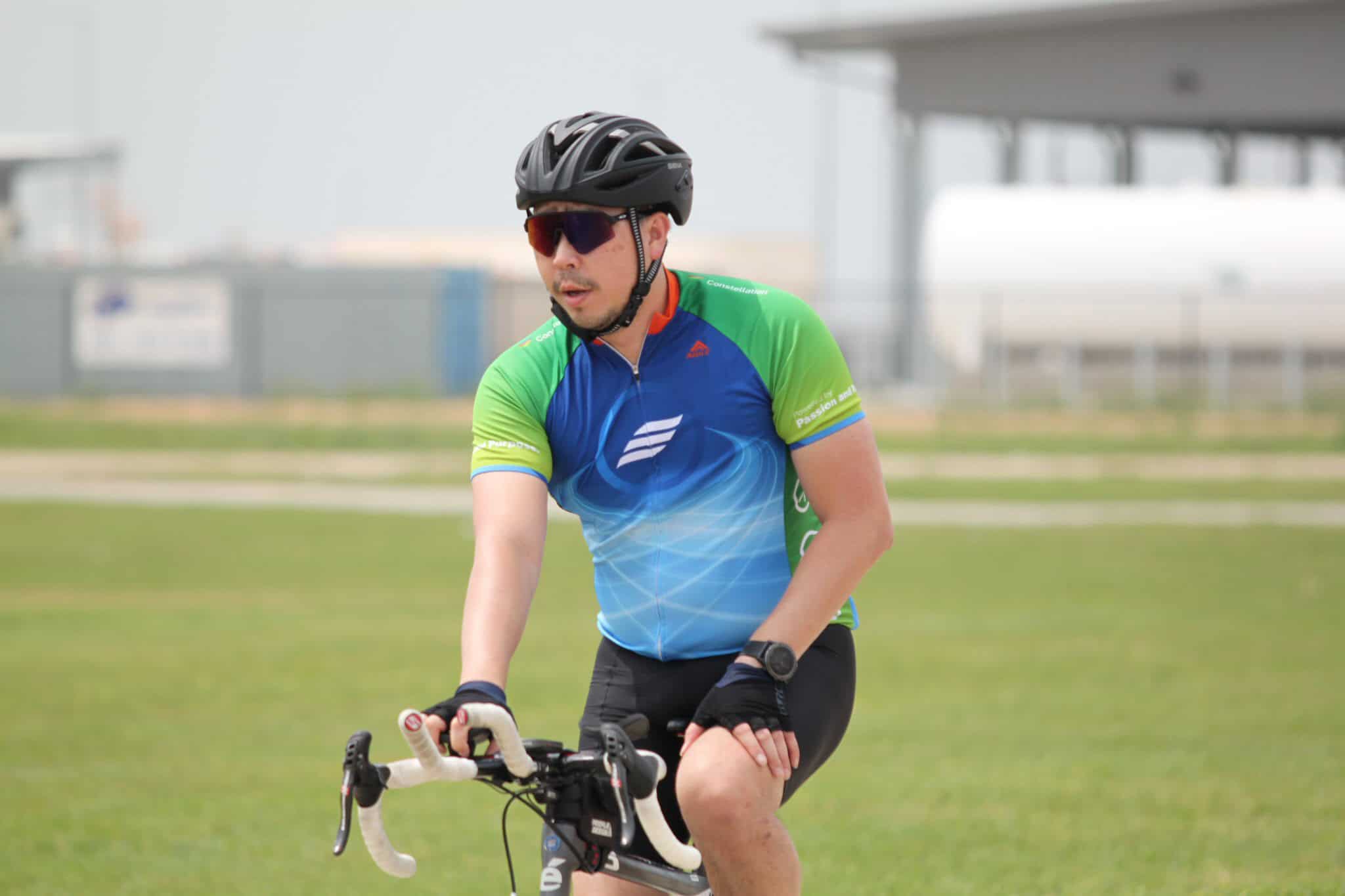 Active cyclist wearing helmet and sunglasses riding a bike outdoors during daytime.