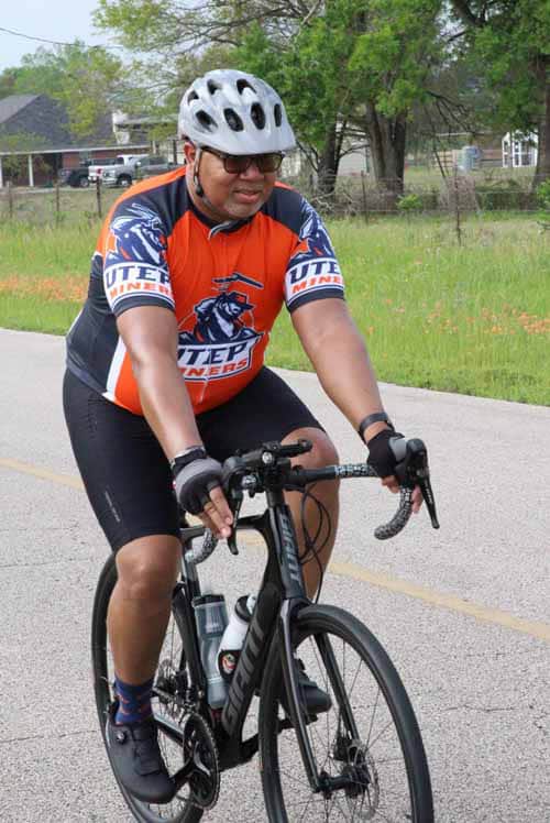 1. Man riding a black road bike wearing a helmet and cycling jersey on a paved path.