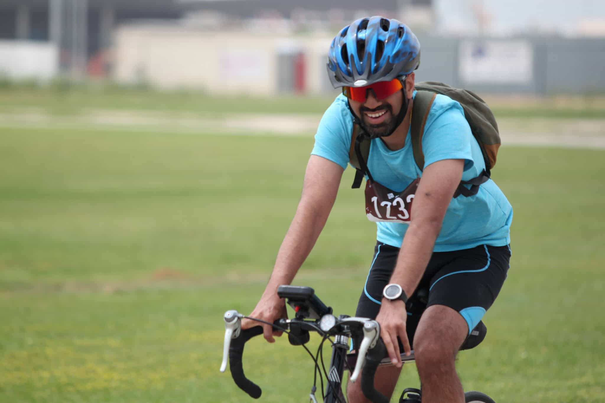 Vibrant male cyclist in blue gear, wearing helmet and sunglasses, racing during a cycling event outdoors.
