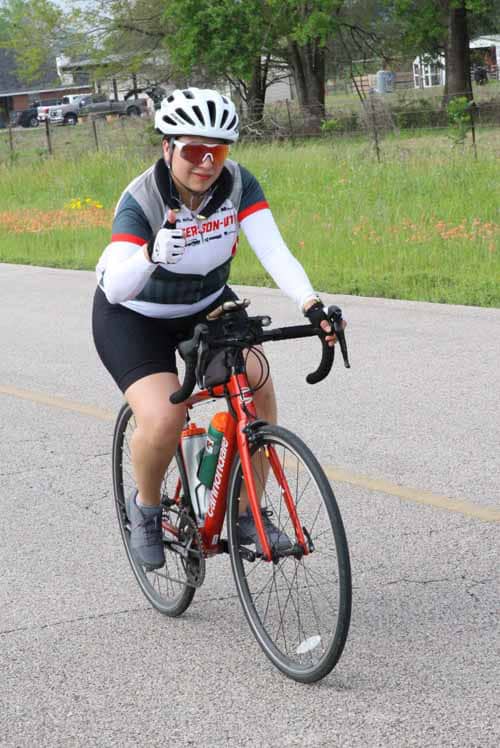 1. Female cyclist riding a red bike on a rural road wearing a helmet and cycling gear.