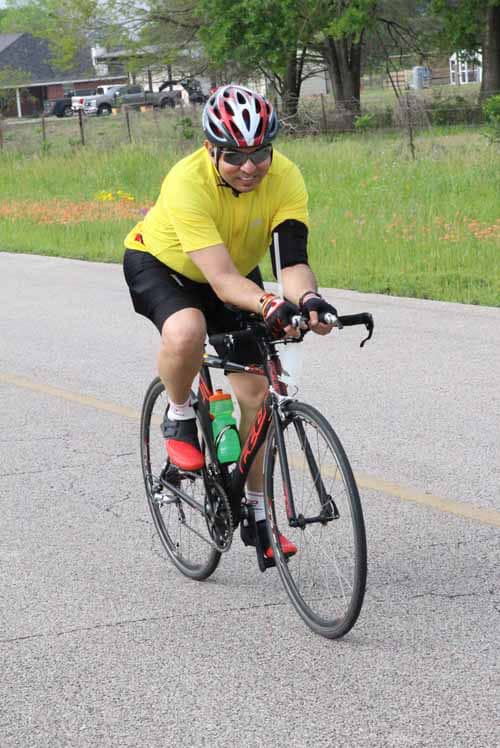Vegan cyclist riding outdoors during daytime in bright yellow jersey and helmet, promoting fitness and eco-friendly travel.