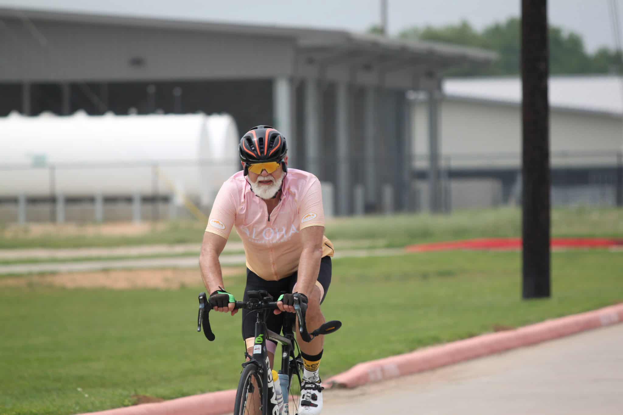 Active senior cyclist riding on a paved path with modern industrial background during daytime.